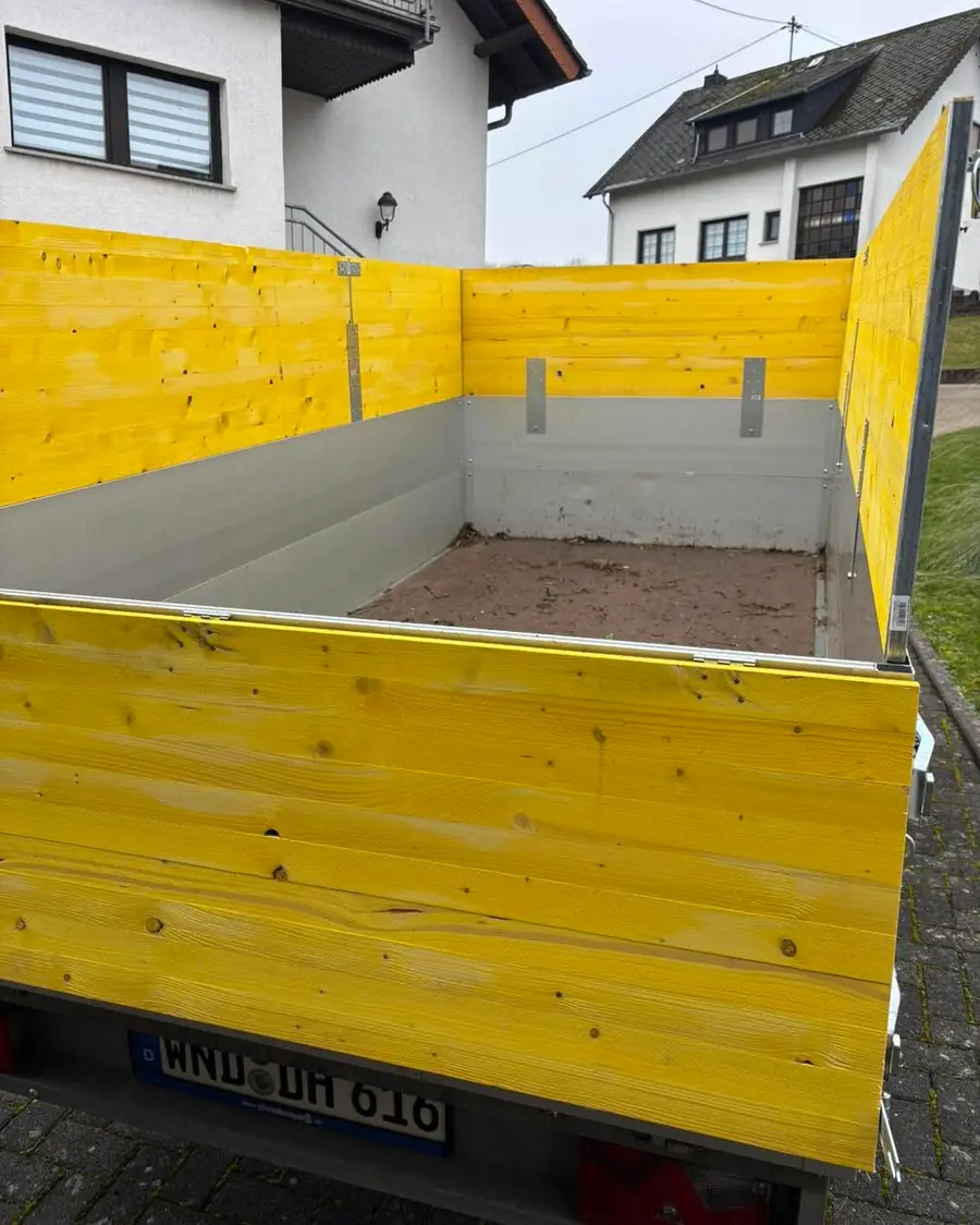 Blick von hinten in den Anhaenger mit fertig montiertem gelbem Holzaufbau im Wohngebiet; am Heck das Kennzeichen 'WND-DH 616' lesb