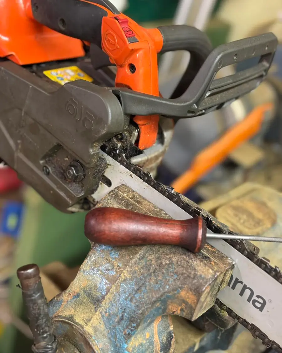 Nahaufnahme einer orangenen Husqvarna-Motorsaege im Schraubstock beim Schaerfen der Saegekette mit Rundfeile; Schriftzug 'Husqvarn
